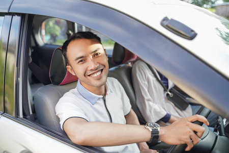 a young asian man laughing looking at the camera while driving in a car while passing on the road