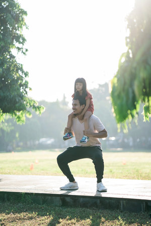 asian father and little daughter do exercises in outdoor. Healthy lifestyle of family with child. dad pushup and child sitting on the backの写真素材