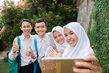 four teenagers in junior high school uniforms taking selfie together using a smartphone on the school groundsの写真素材