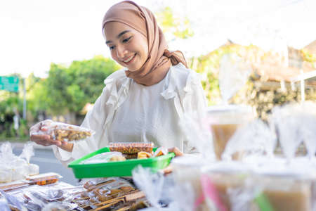 A beautiful girl in a headscarf holding a snack wrapped in plastic will be bought at a roadside stallの写真素材