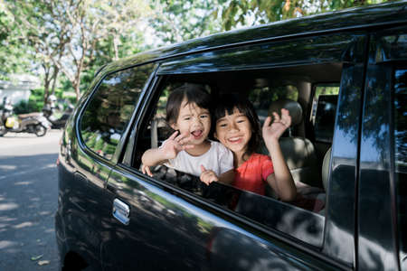 Happy asian siblings waving hands from window and travel by carの写真素材