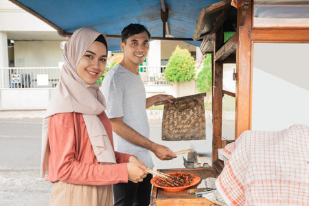 two seller preparing food on their food stall selling traditional chicken satay. asian sate ayam...
