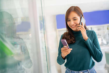 beautiful woman making a call with a smartphone while choosing cell phone accessories in a cell phone shop on a glass display case backgroundの写真素材