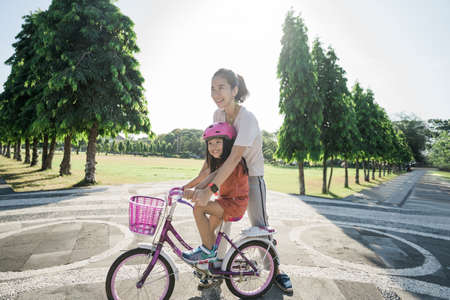 portrait of asian mother Teaching daughter To Ride Bike In the parkの写真素材