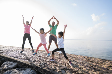 asian parent and children jumping up and down sport. healthy family stretching and exercise in the morningの写真素材