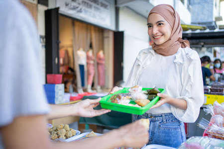 A beautiful girl in a veil give a plastic tray of food eaten upon breaking the fast to seller at a roadside stallの写真素材