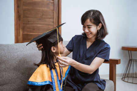 Kindergarten graduation. Asian mother and kid preparing on her kinder graduate day at homeの写真素材