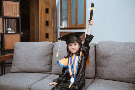 Kindergarten graduation. proud kid on graduation day raise her arm with sertificate