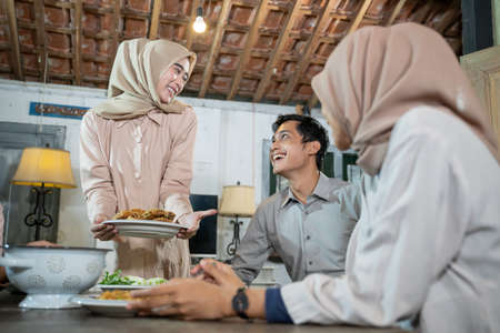 a girl in hijab brings a plate of fried chicken to eat together when gathering with friends in the dining roomの写真素材