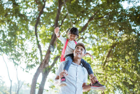 daughter sitting on fathers shoulder when going to school in the morningの写真素材
