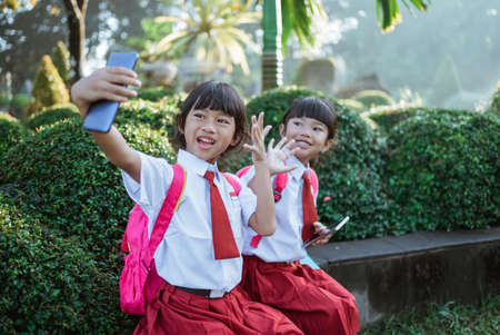 two best friend of indonesian primary school student take selfie together in the parkの写真素材