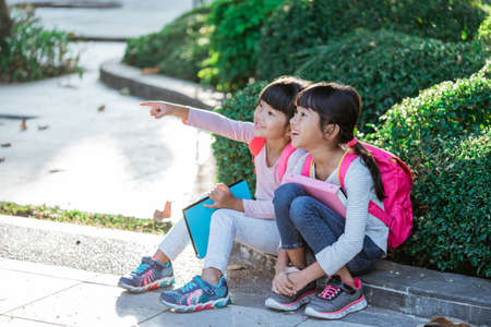 cute two asian student in uniform pointing away while sitting togehter in the parkの写真素材