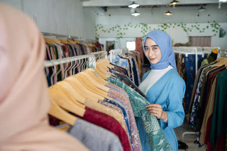 a business woman wearing a blue veil using a tablet while holding clothes on a hanger at a Muslim clothing storeの写真素材