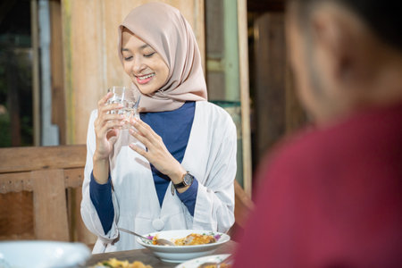 a smiling veiled woman holding a glass while drinking for iftar in the dining roomの写真素材