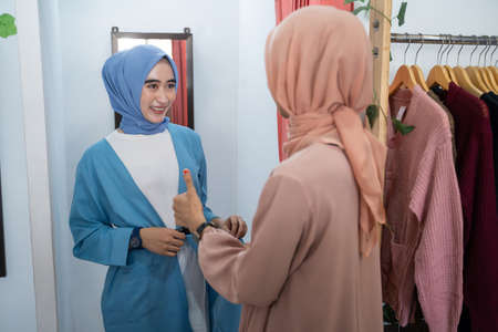a woman in a veil tries on clothes in a changing room in front of the mirror and her friend compliments her with a thumbs up at a boutique shopの写真素材