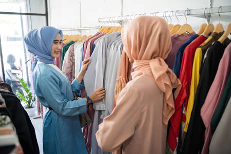 a female customer in a veil chooses clothes when a waiter serves her when choosing clothes on a hanger at a boutique shopの写真素材