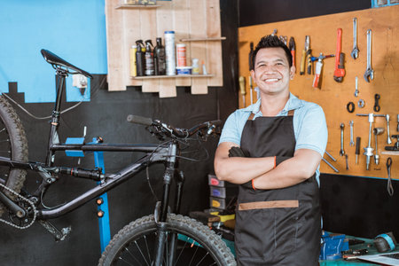 A bicycle mechanic wearing an apron and gloves smiles with crossed hands