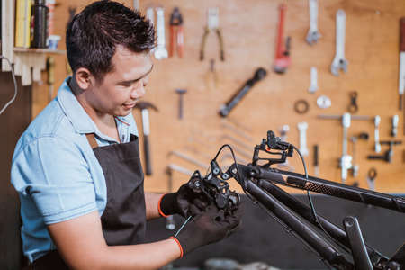 a mechanic wearing an apron and gloves installs the rear derailleur with cableの写真素材