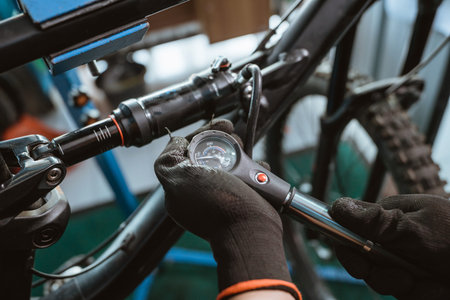 close up of a bicycle mechanics hand in gloves using a pressure gauge pump to adjust the suspension