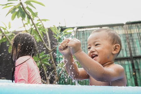 cheerful little boy playing water in the outdoor pool with siblingの写真素材