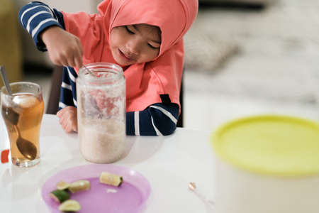 portrait of a little girl in a hijab spooning sugarの写真素材