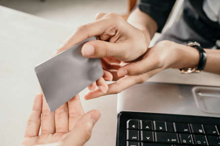 Close up of woman hands giving credit or debit card to man for transaction in officeの写真素材