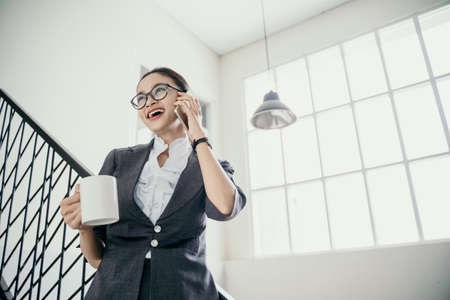 young beautiful businesswoman talking on the phone happy while hold drinkの写真素材