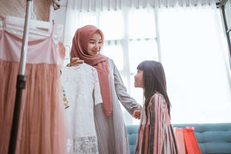 mother muslim choosing a dress for her daughter at clothing storeの写真素材