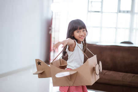 girl playing with cardboard toy airplane at homeの写真素材