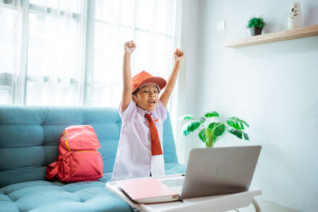 excited primary school student with uniform raise her arm during online classの写真素材