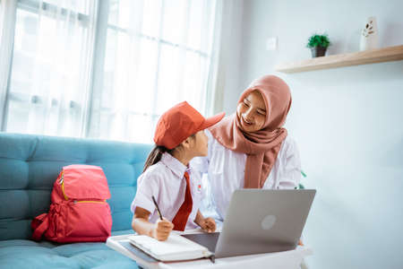 asian muslim primary student with mother sitting together doing homework at homeの写真素材