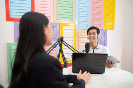 a male presenter chats with a woman using a microphone during a podcastの写真素材