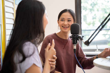side view of two girls laughing while having a dialogue on a podcast show using a microphoneの写真素材