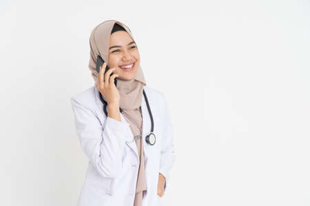veiled doctor wearing white suit uniform listening on a call using a mobile phone happily with copyspaceの写真素材