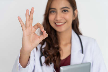 close up of attractive female doctor smiling teeth in uniform with okay symbol gesture while holding padの写真素材