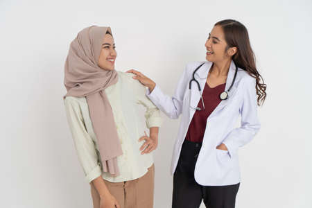 smiling woman in headscarf and beautiful female doctor happy looking at each other and standing side by sideの写真素材