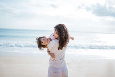 mother swinging her toddler daughter playing in the beachの写真素材