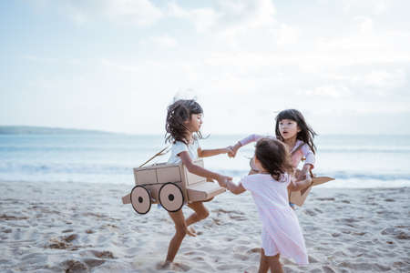 sibling and girl friend playing with cardboard airplane and car on the beachの写真素材