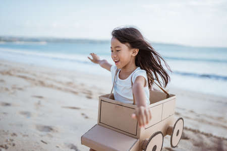 Daughter playing with cardboard airplane on the beachの写真素材