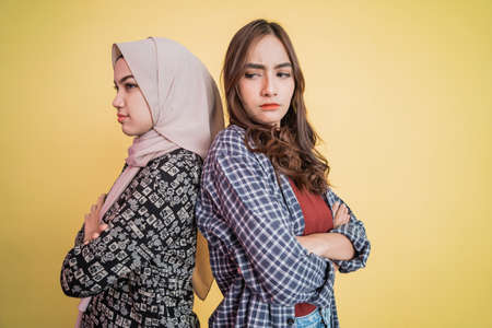 close up of two sad girls standing back to back and crossed handsの写真素材