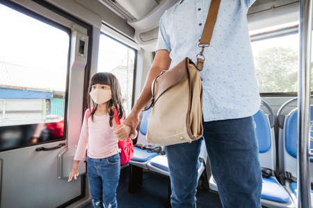 asian father taking his daughter to school by riding bus public transport wearing a face maskの写真素材