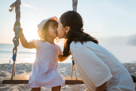 daughter kissing her mother while swinging at the beachの写真素材