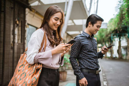 man and woman standing on a sidewalk smiling using their phoneの写真素材