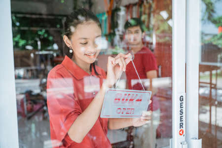 a woman in a red t-shirt prepares to open a shop by posting an open sign on the windshield doorの写真素材