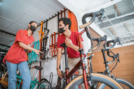 a young mechanic fixing seatpost and a saleswoman in mask check a new bicycle parts for customerの写真素材