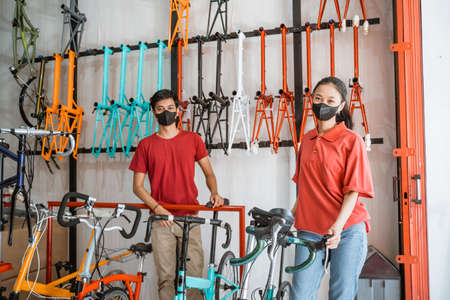 saleswoman and salesman in black mask looking at camera in bicycles shopの写真素材