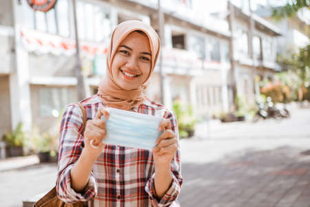 asian muslim woman showing mask while standing outdoorの写真素材