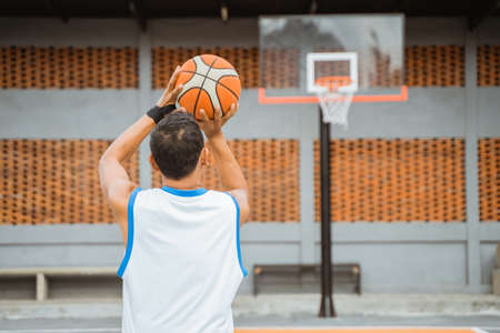 back view of a male basketball player holding the ball while shooting at the hoopの写真素材