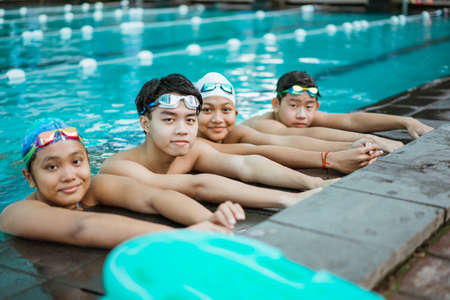 four smiling teenagers in swimsuits while resting by standing by the poolの写真素材