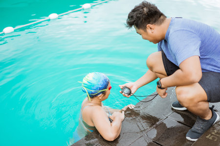 a male trainer showing the time with a stopwatch to a teenage swimming athleteの写真素材